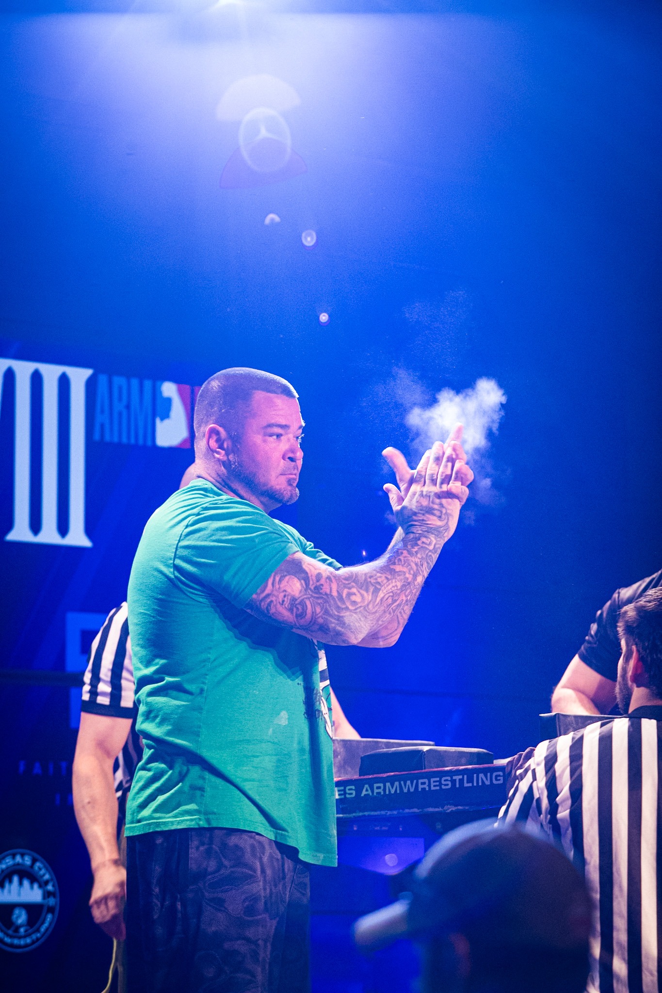 A puller chalking his hands under blue stage lights before a match